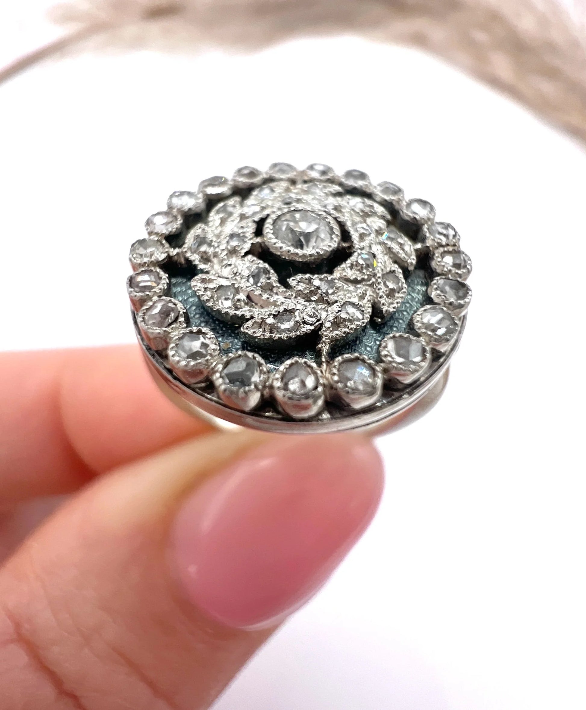 A diamond and dark blue enamel fancy cluster ring in white gold, held in a hand