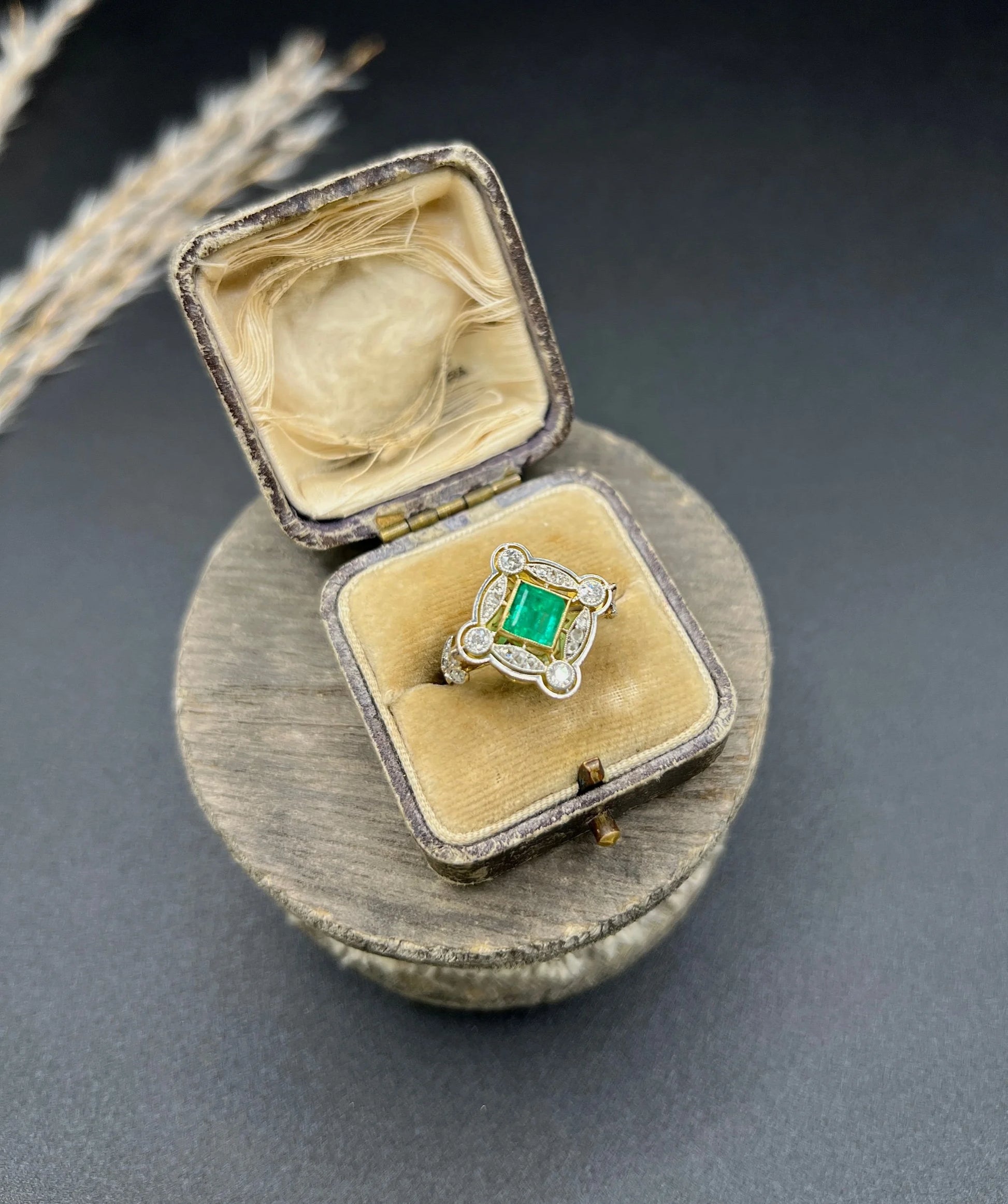 A gold and platinum ring with a centre emerald and diamond surround, in an antique ring box