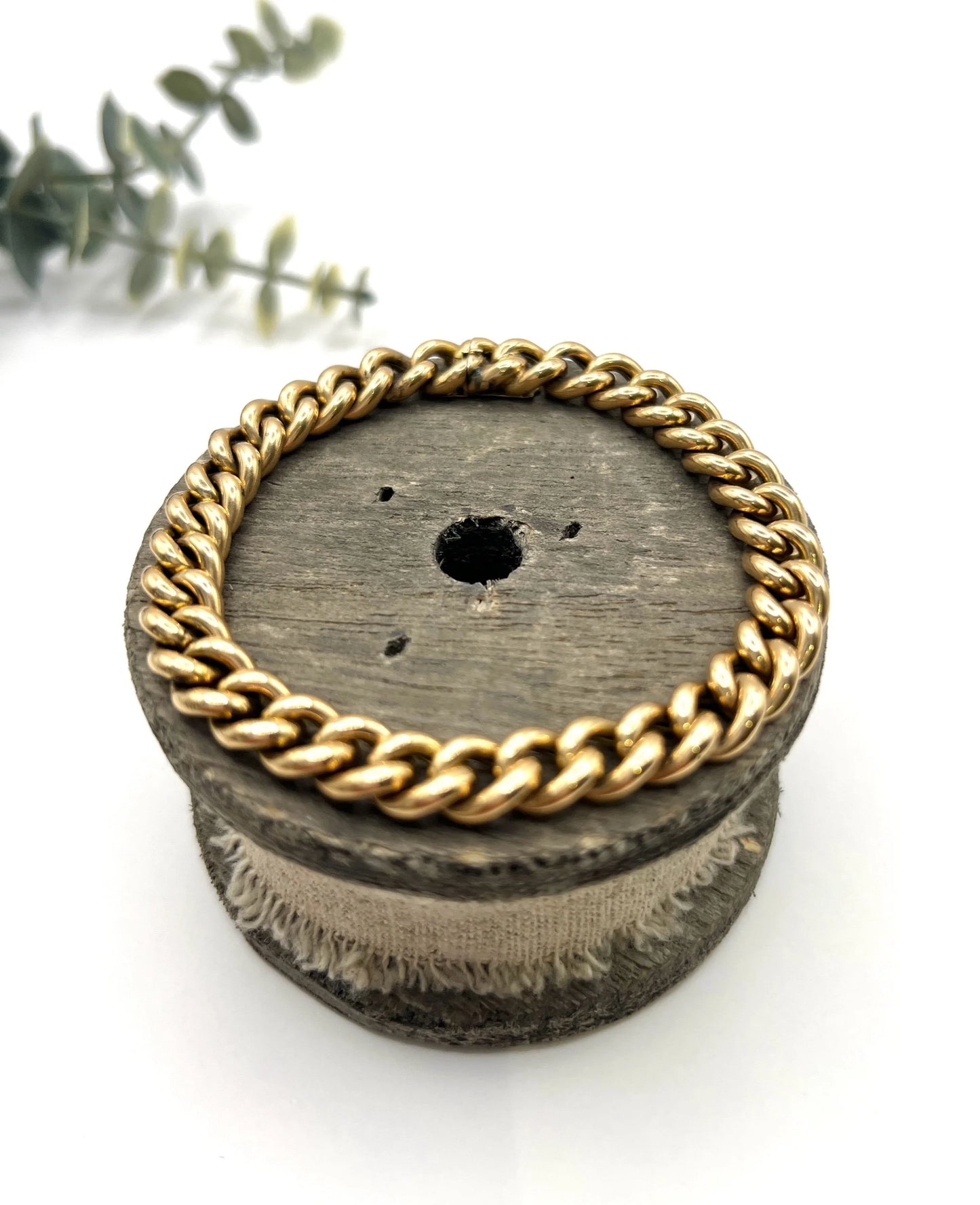 A curb link bracelet in yellow gold, on a wooden spool