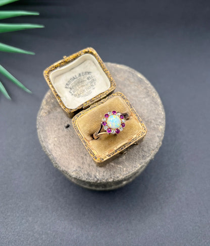 A daisy style cluster ring in rose gold with opal, ruby and diamond, in an antique ring box