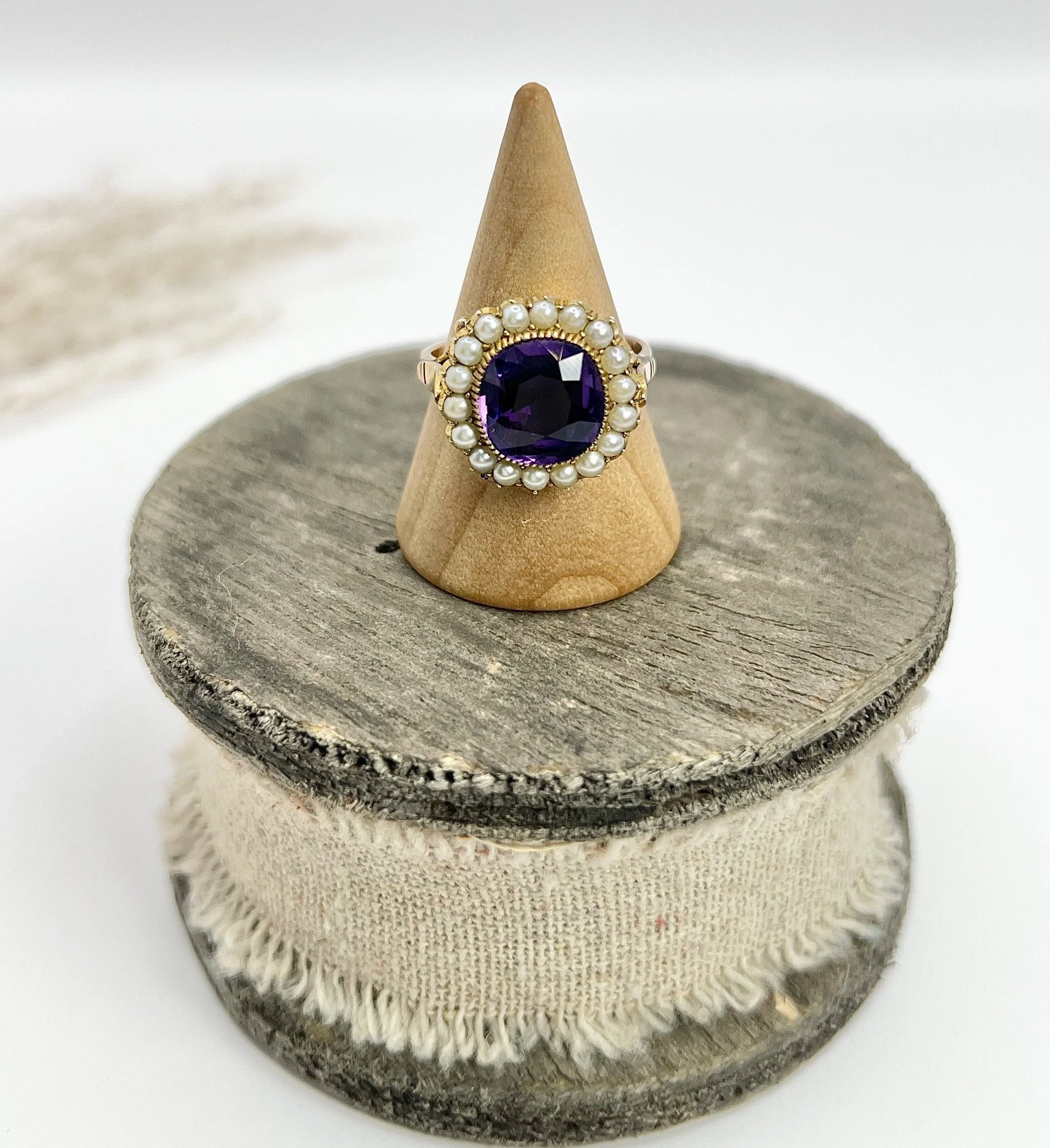 A cushion shaped amethyst cluster ring with a pearl border, in yellow gold, on a ring cone