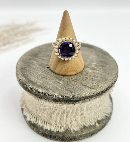 A cushion shaped amethyst cluster ring with a pearl border, in yellow gold, on a ring cone