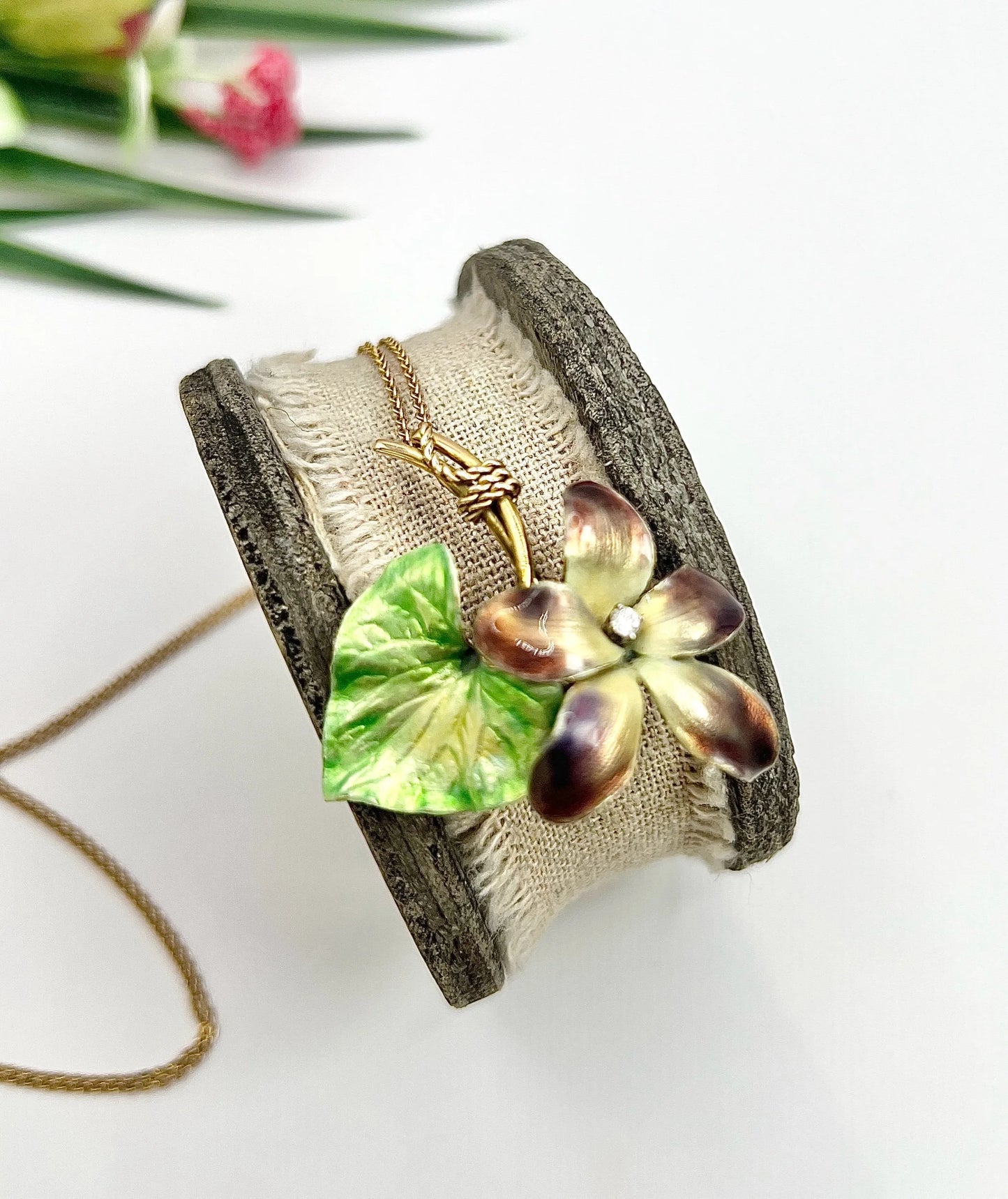 An enamelled flower pendant with gold chain, on top of a wooden and cloth object