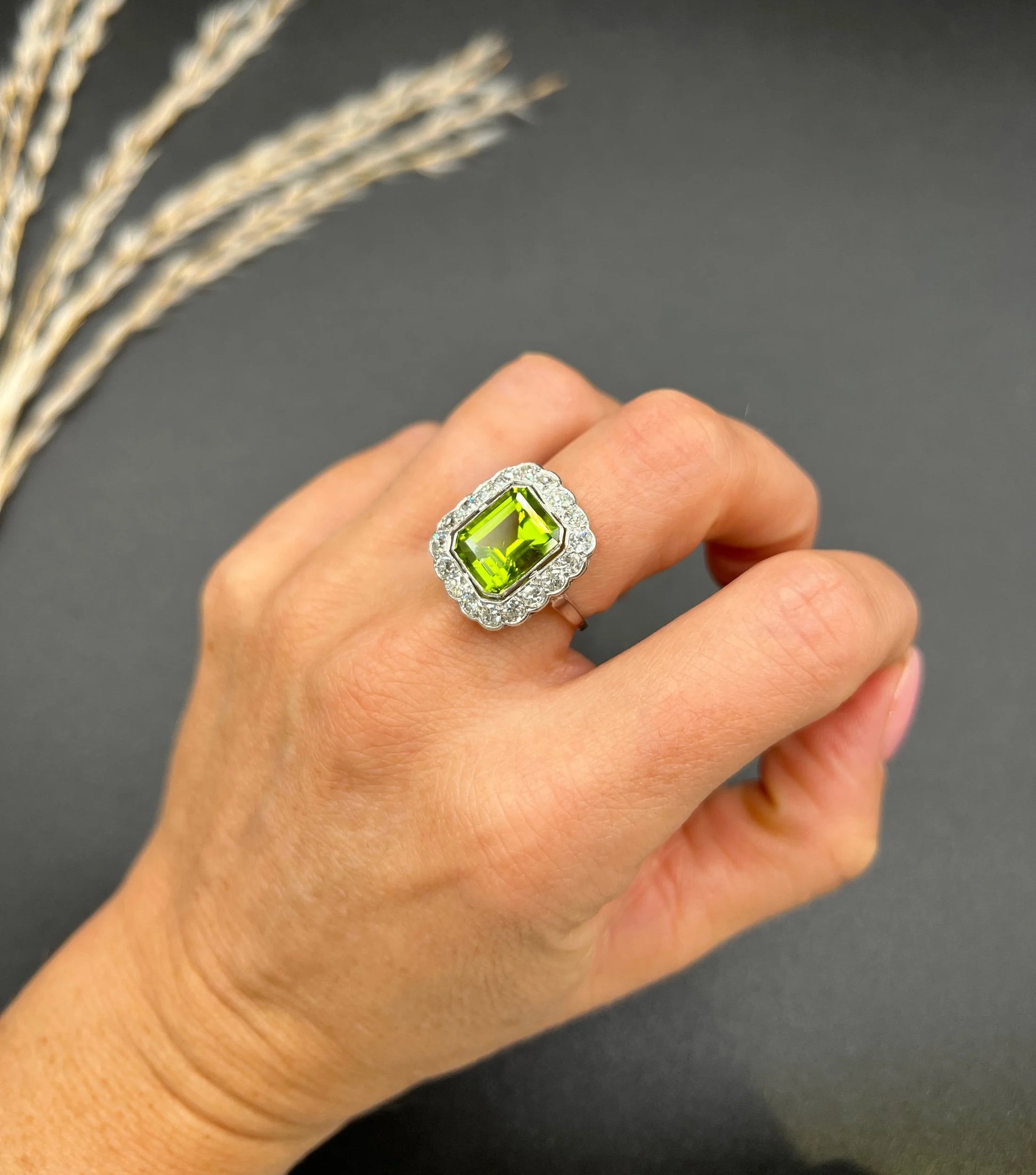 A cushion shaped peridot and diamond cluster ring in white metal, modelled on a hand