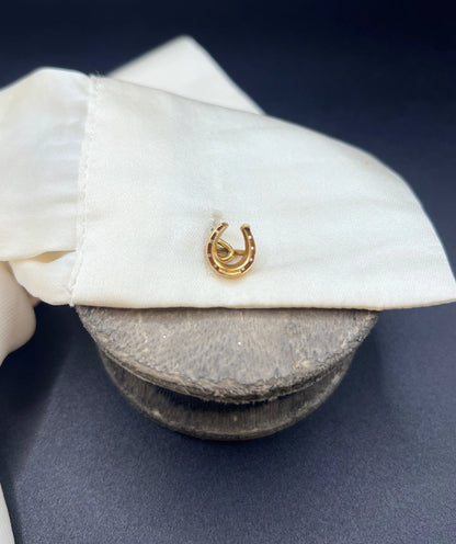 A double-sided horseshoe cufflink in yellow gold, modelled in a white shirt cuff