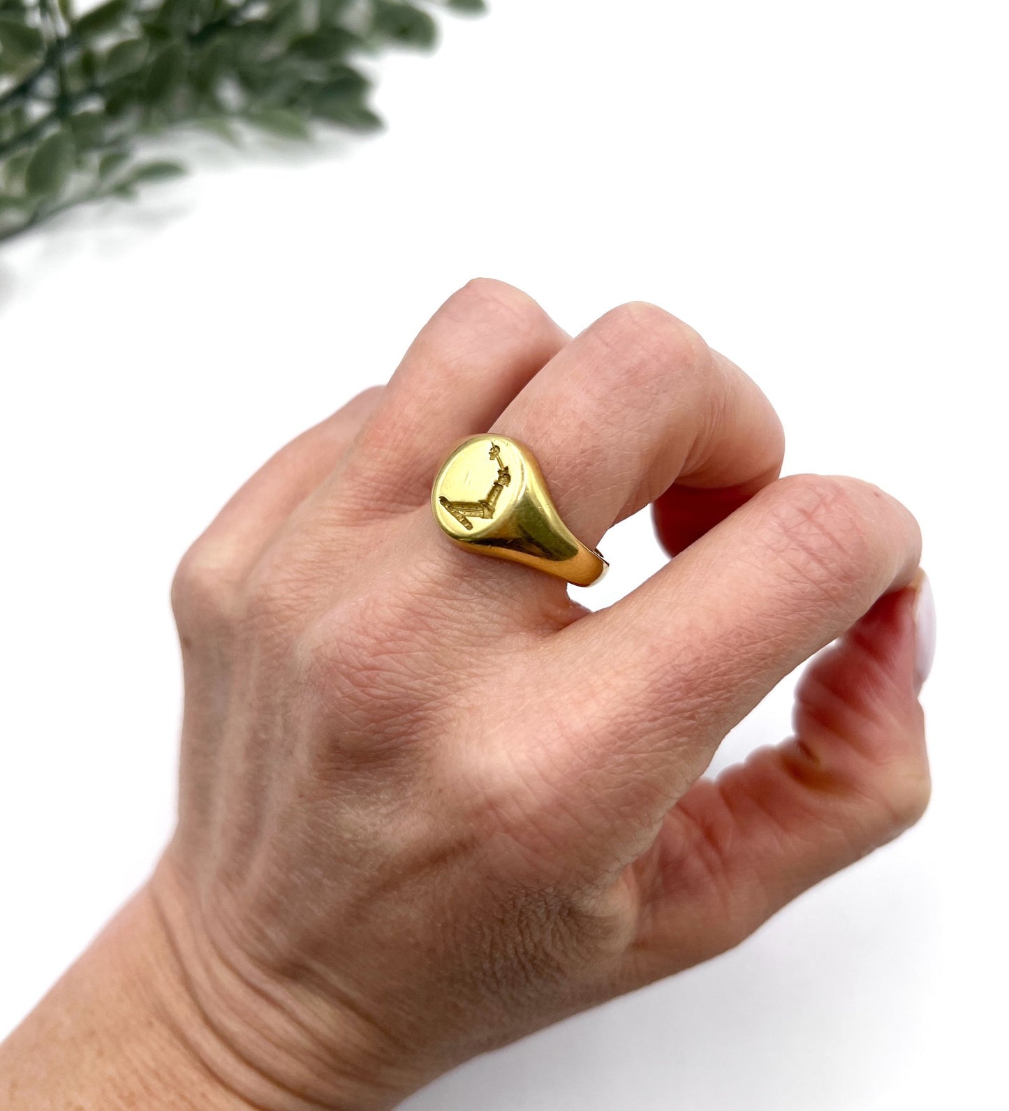 A yellow gold oval signet ring with a seal engraved heraldic crest, modelled on a hand