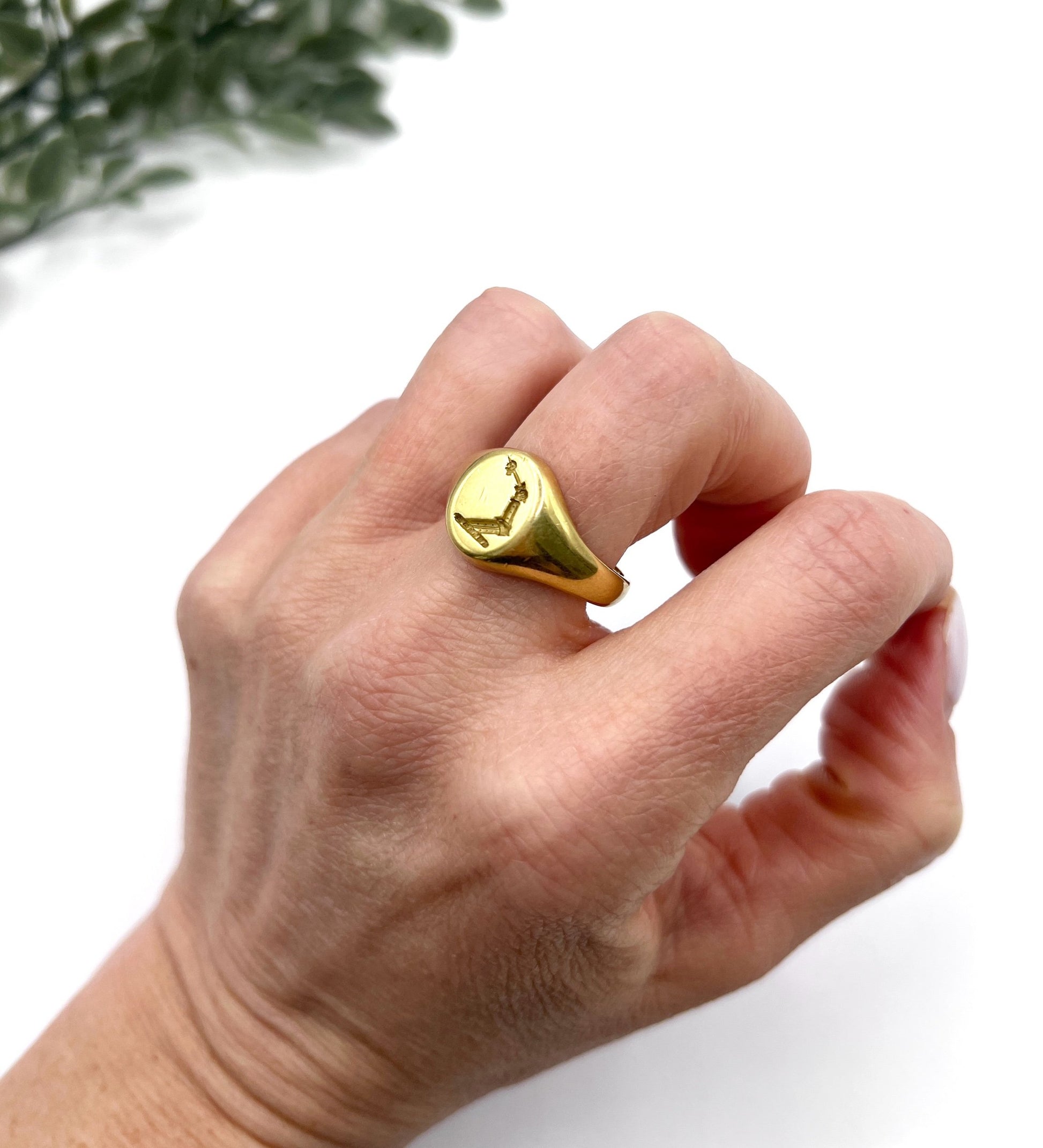 A yellow gold oval signet ring with a seal engraved heraldic crest, modelled on a hand