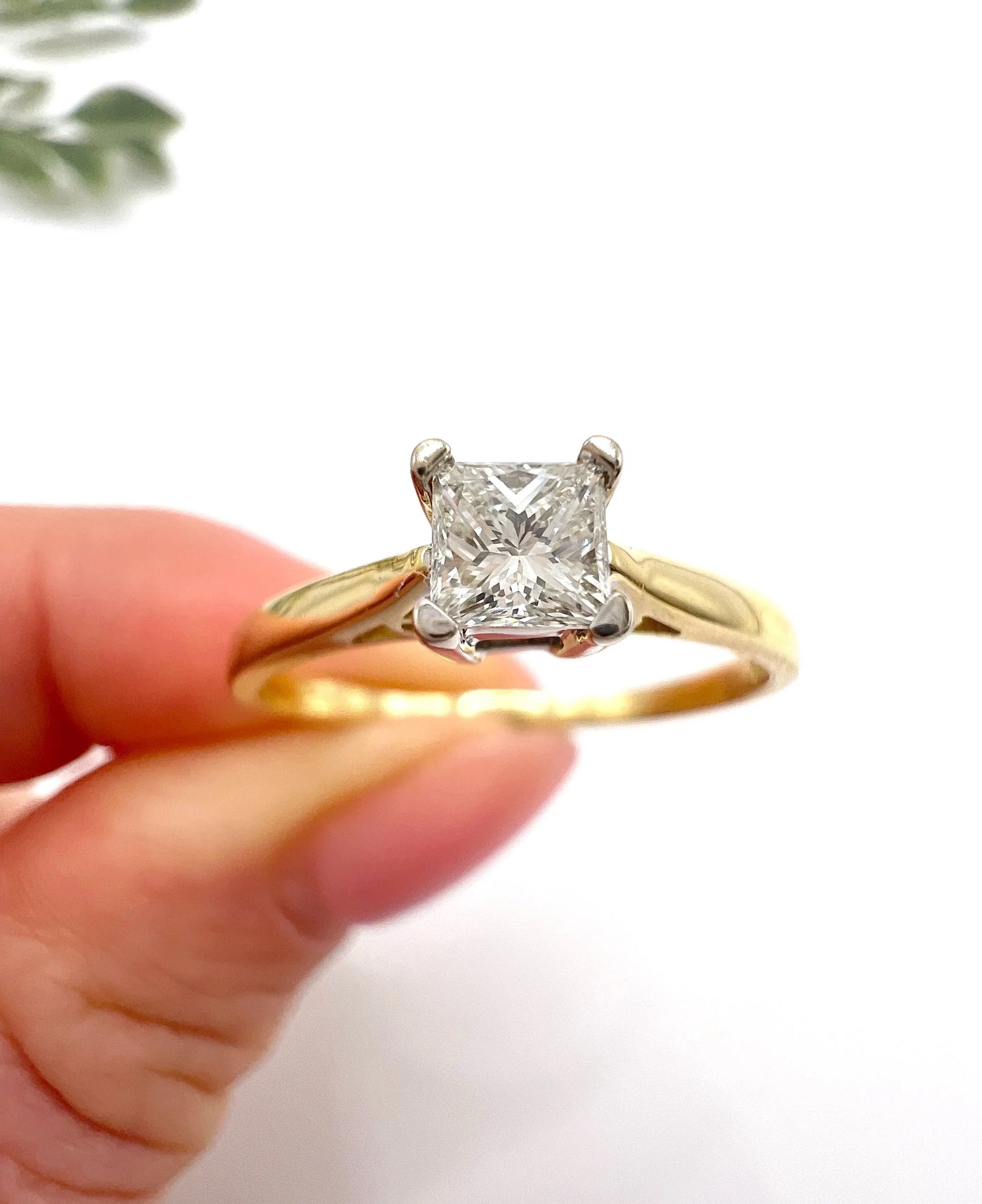 A solitaire princess cut diamond ring in yellow and white gold, held in a hand