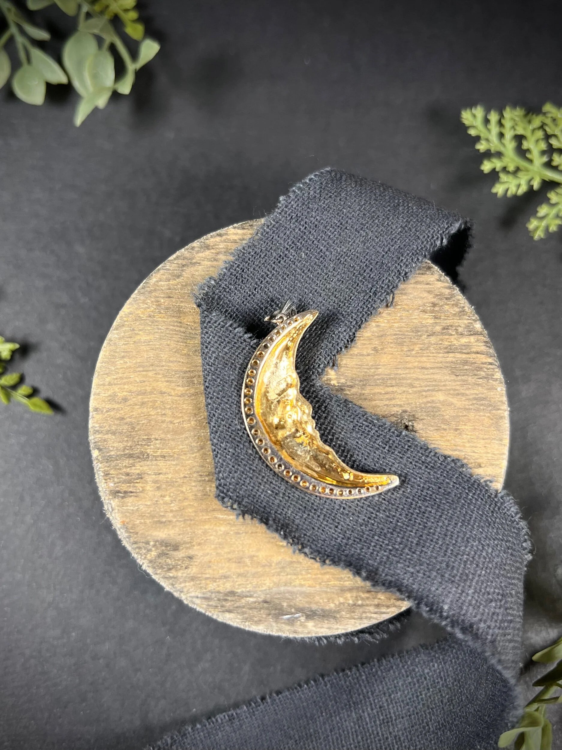 A gold crescent moon pendant with diamonds, on a black ribbon
