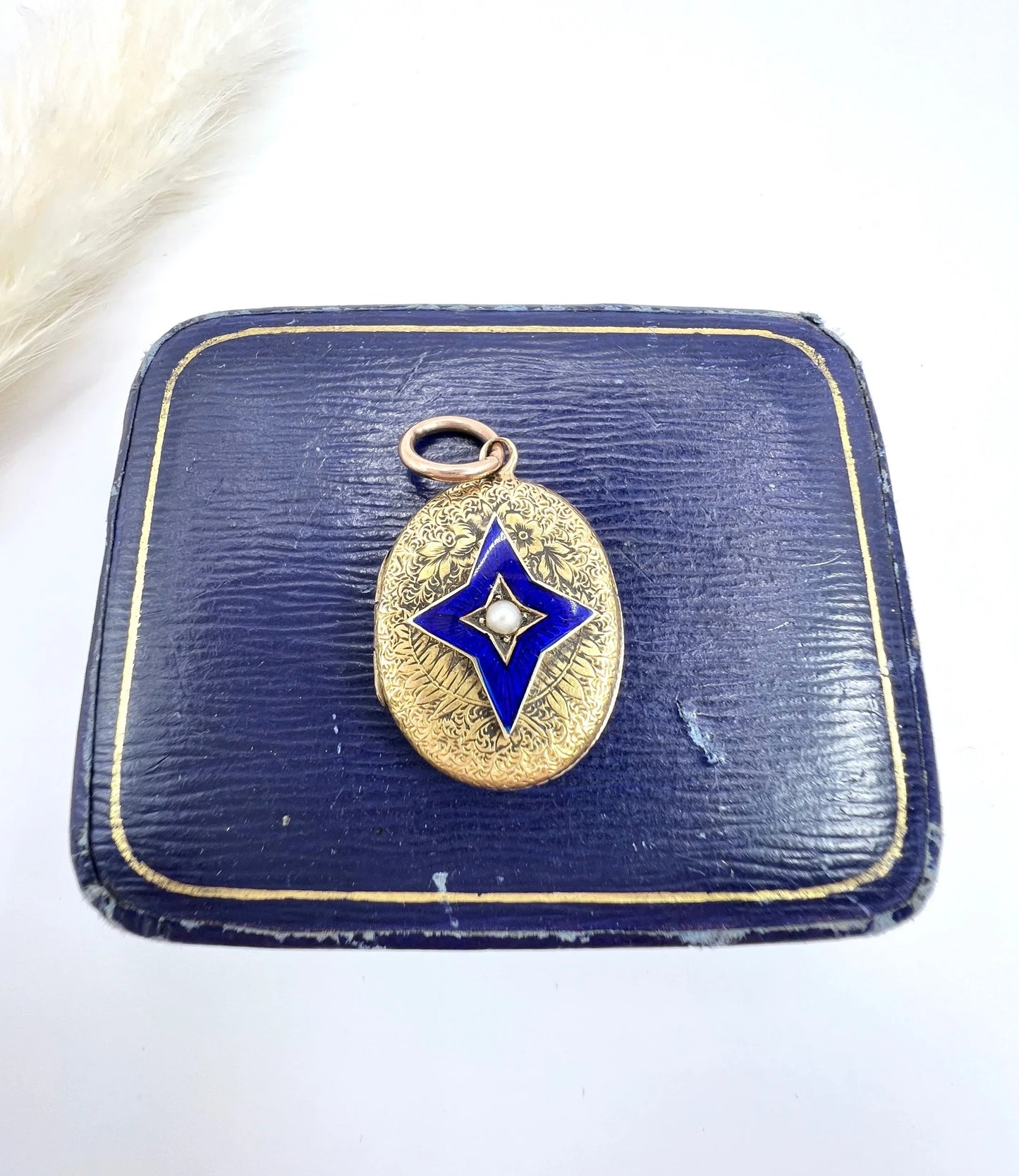 An oval yellow gold locket with a blue enamel star and seed pearl centre