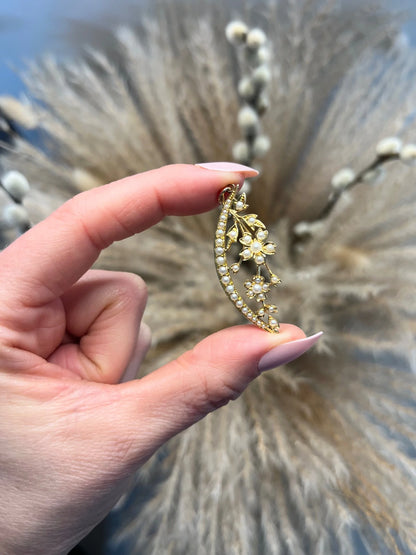 A yellow gold floral crescent pendant with pearls, held in a hand