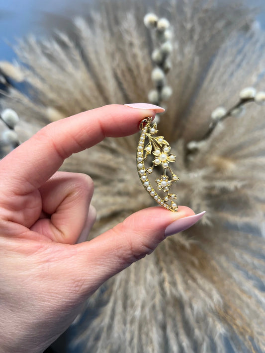 A yellow gold floral crescent pendant with pearls, held in a hand