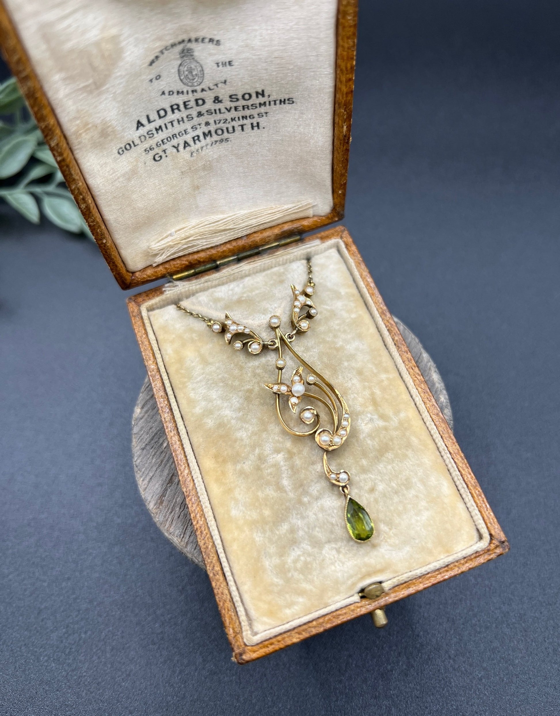 A yellow gold floral pendant necklace with pearls and a peridot drop, in an antique box