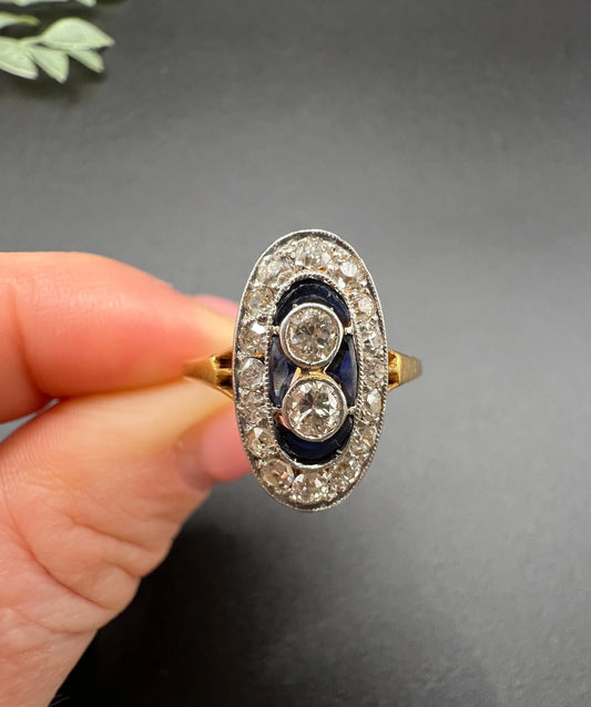 An oval cluster ring with diamonds and sapphires in platinum and yellow gold, held in a hand