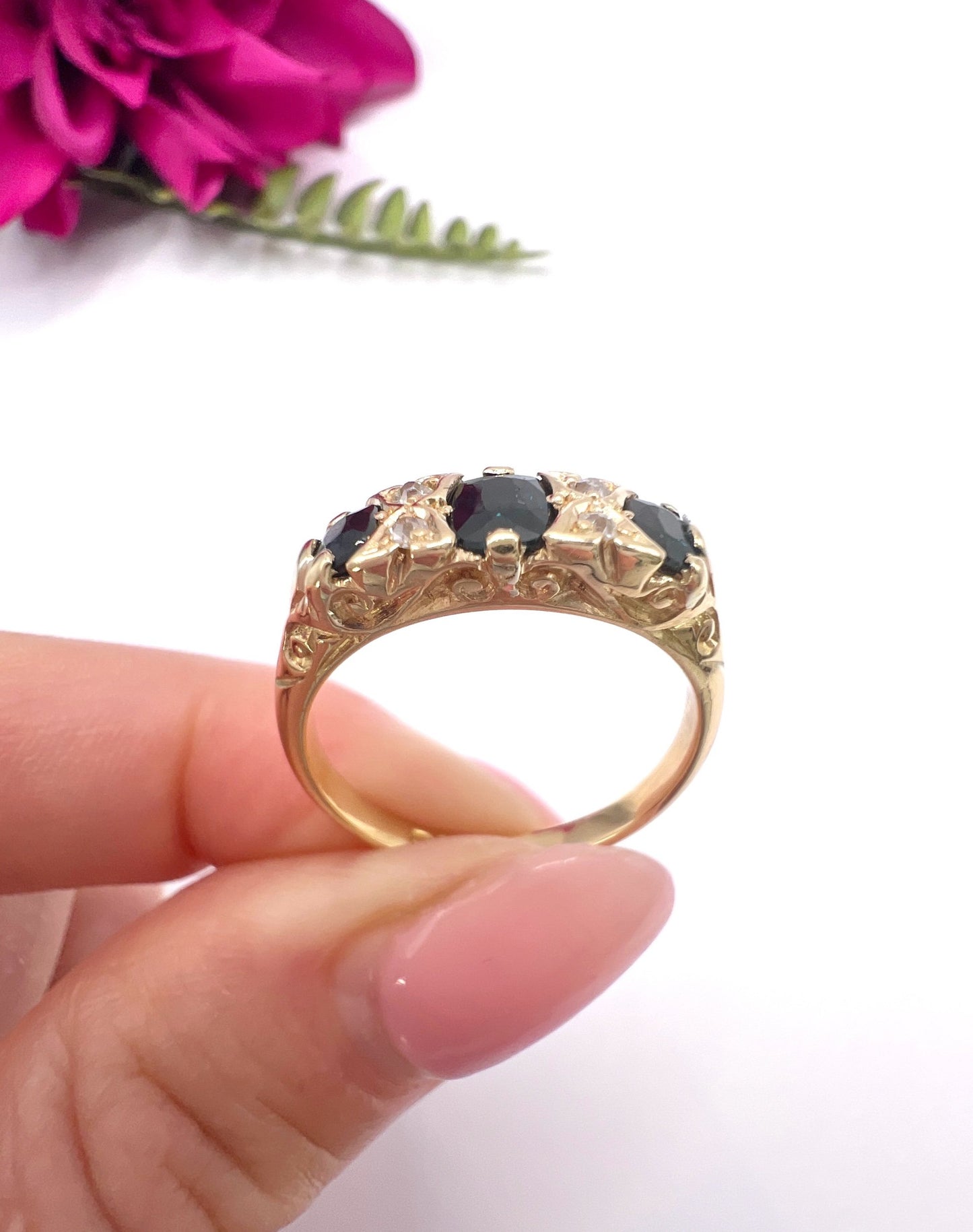 A seven stone sapphire and diamond carved ring in yellow gold, held in a hand