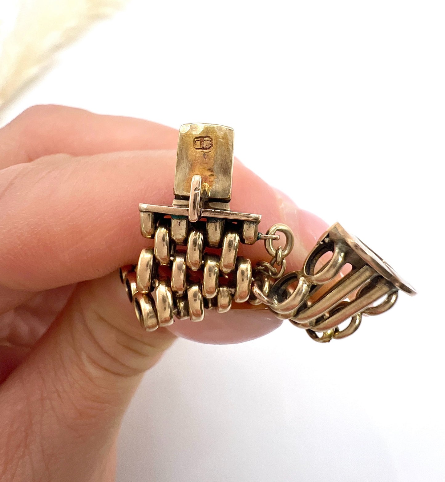A close-up of a bracelet clasp stamped 15, held in a hand