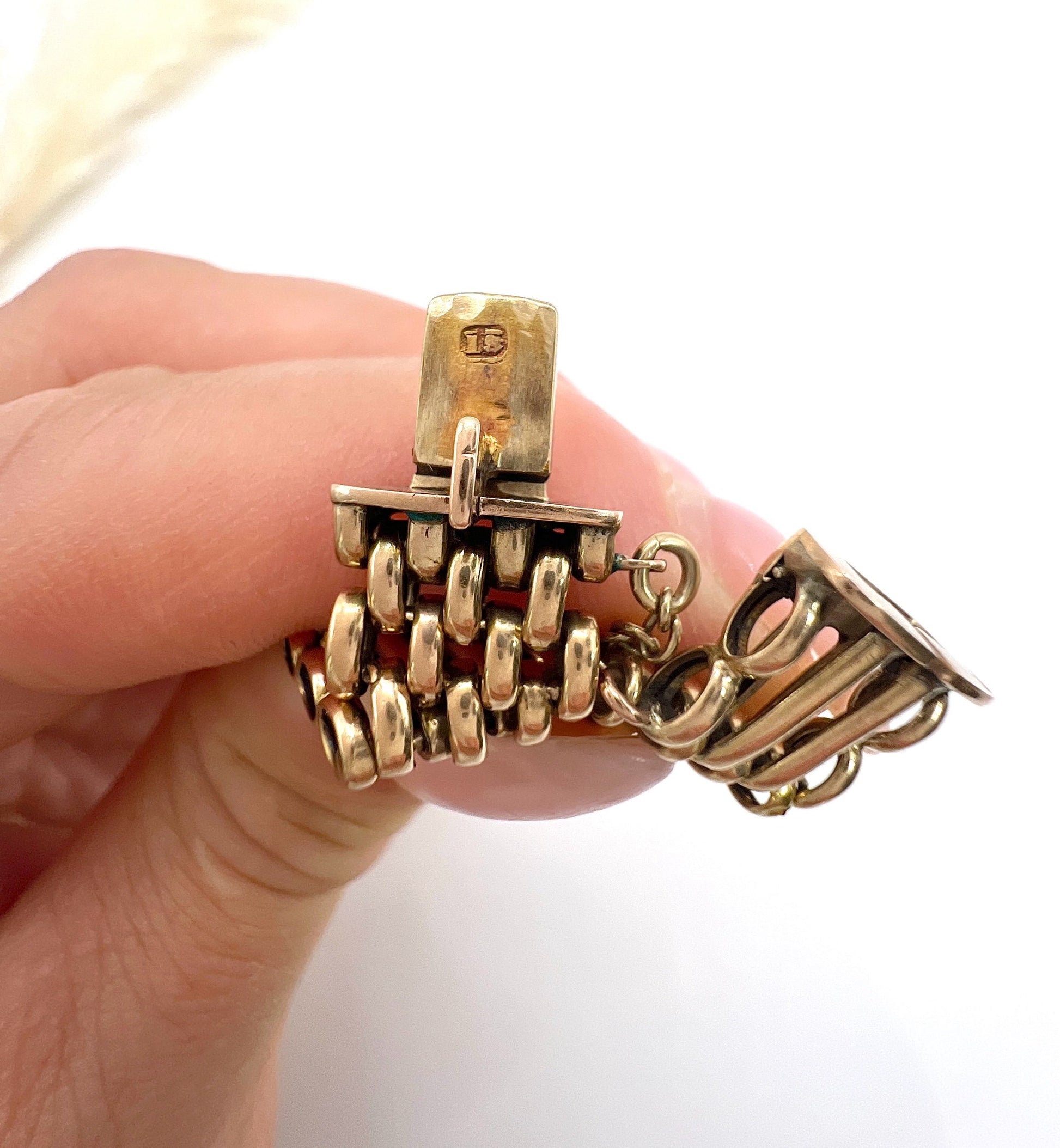A close-up of a bracelet clasp stamped 15, held in a hand