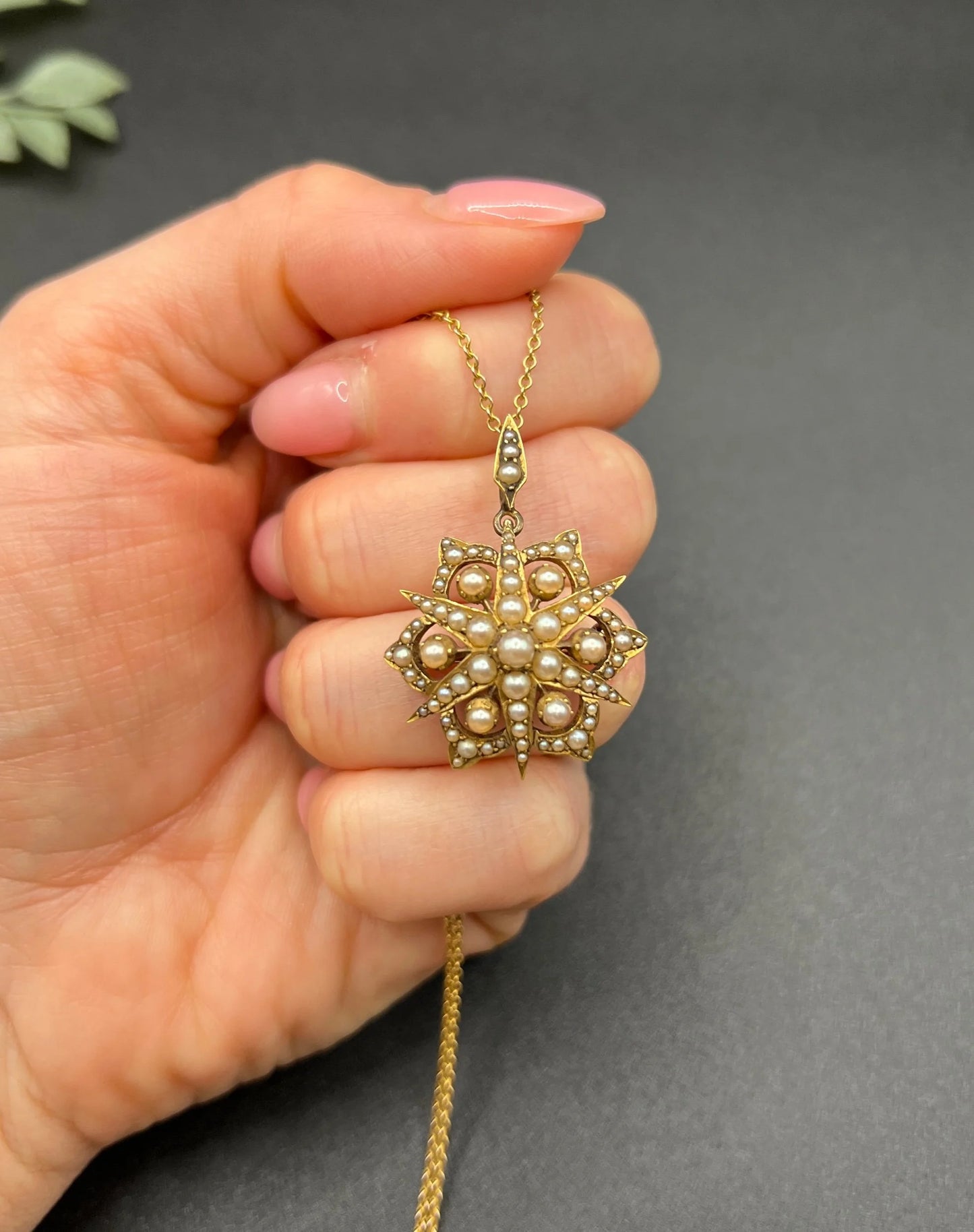 A yellow gold brooch/pendant with pearls in the shape of a star, with a chain, held in a hand