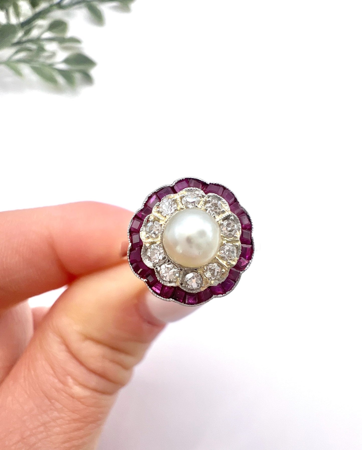 A pearl, diamond and ruby fancy cluster ring in platinum and yellow gold, held in a hand