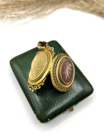 A yellow gold ornate cherub cameo locket pendant, open, on top of an antique box