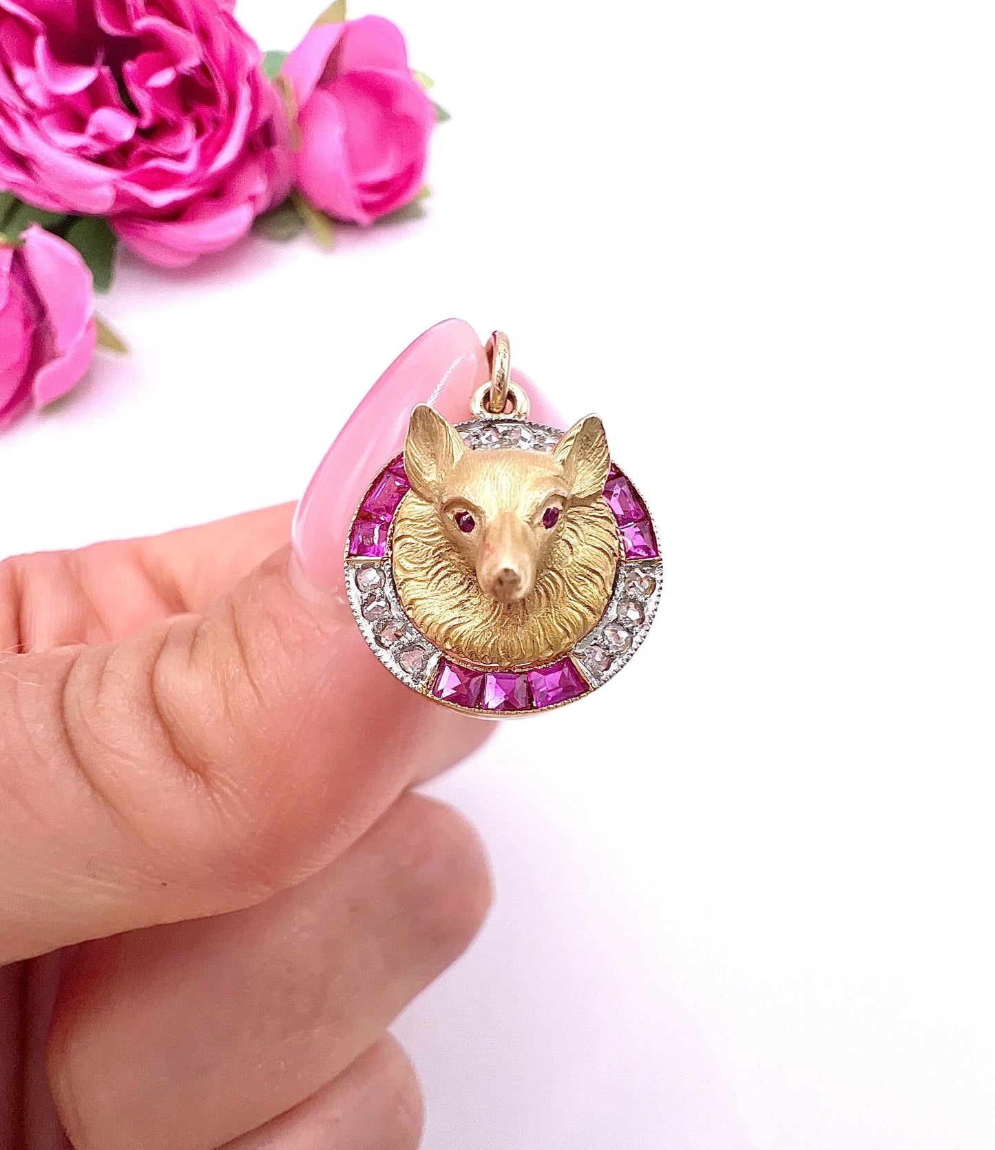 A fox head pendant in yellow gold with a ruby and diamond border, held in a hand