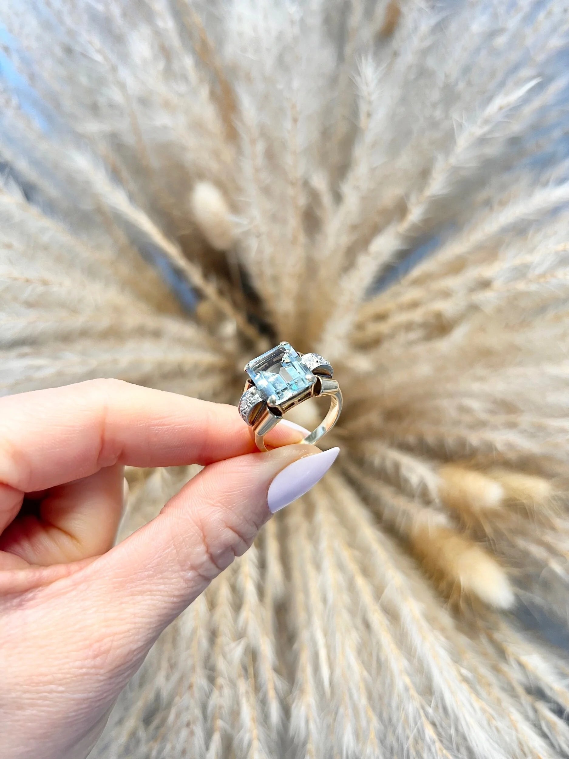 An aquamarine and diamond cocktail ring in gold, held in a hand