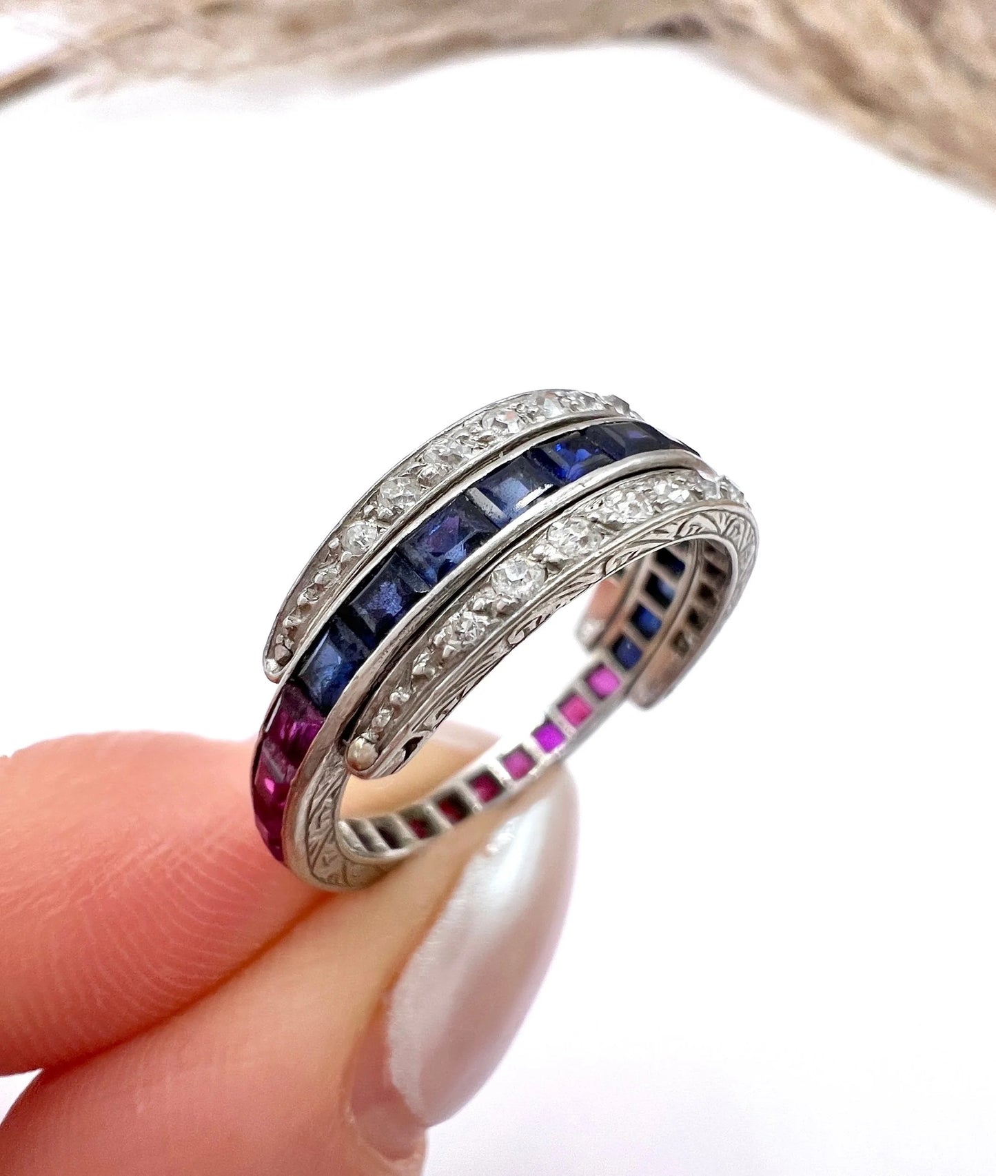 A platinum night and day flip band ring set with diamonds, sapphires and rubies, held in a hand