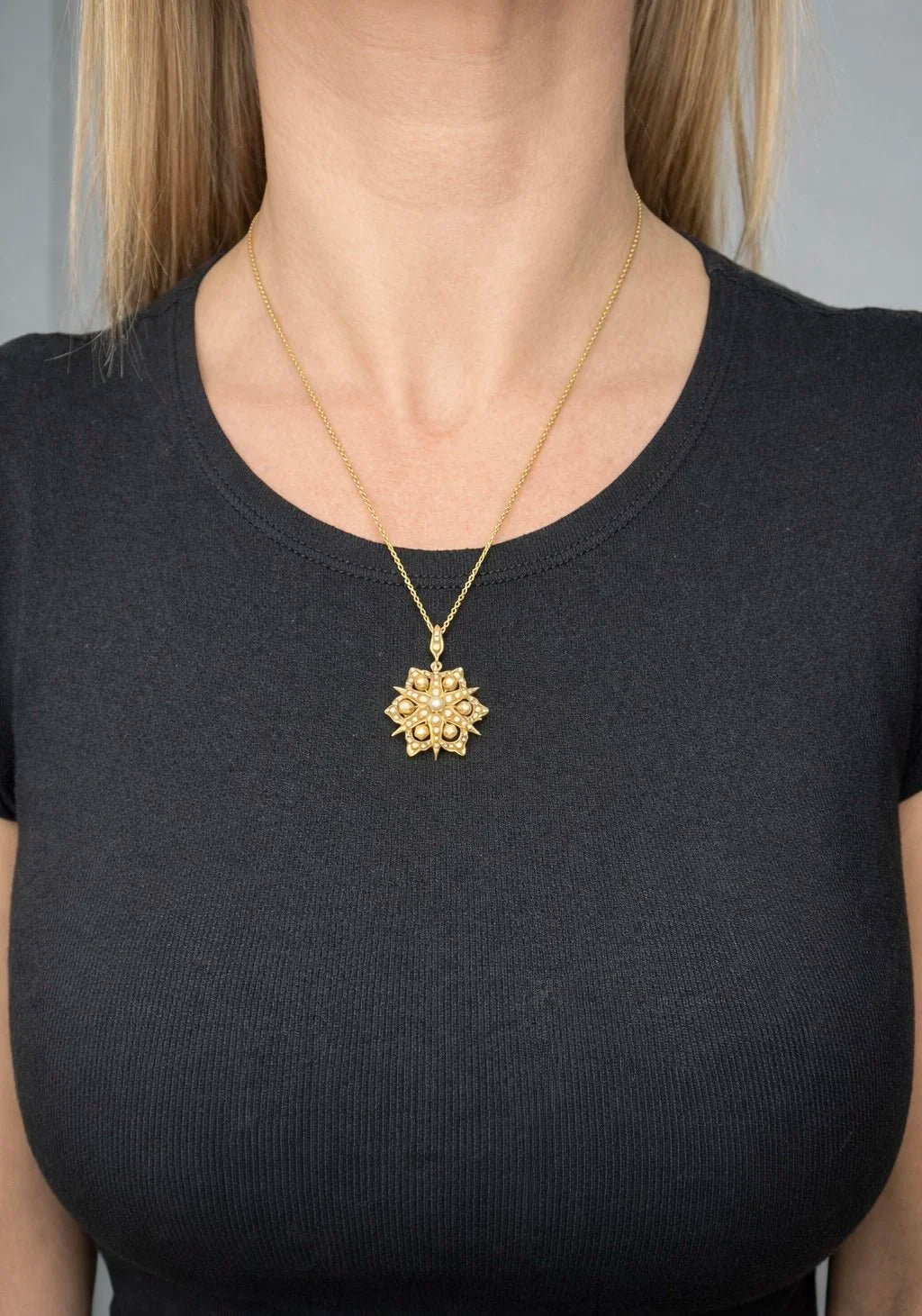 A yellow gold brooch/pendant with pearls in the shape of a star, with a chain, modelled by a woman wearing a black top