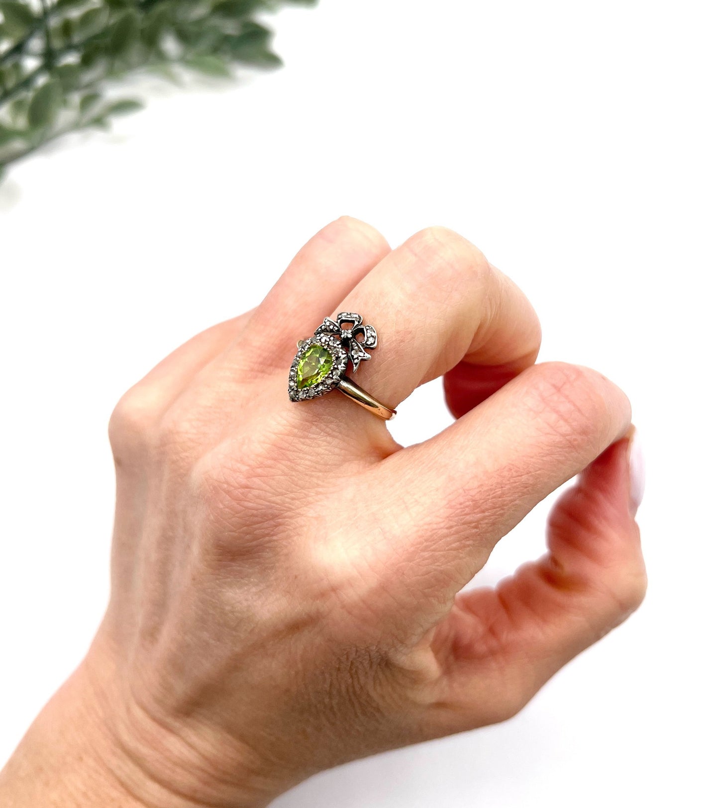 A pear cut peridot and round diamond cluster ring with bow detail, in yellow gold and white metal, modelled on a hand