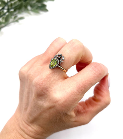 A pear cut peridot and round diamond cluster ring with bow detail, in yellow gold and white metal, modelled on a hand