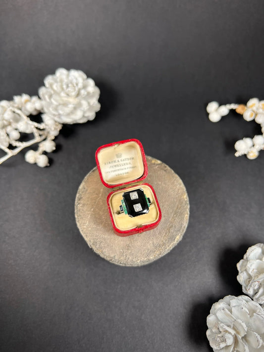 A geometric black onyx ring with diamonds and emeralds in white gold, in an antique ring box