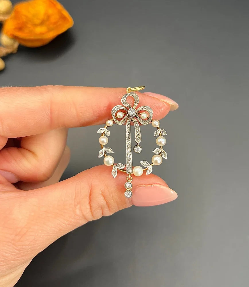 A pearl and diamond bow pendant in gold and platinum, held in a hand