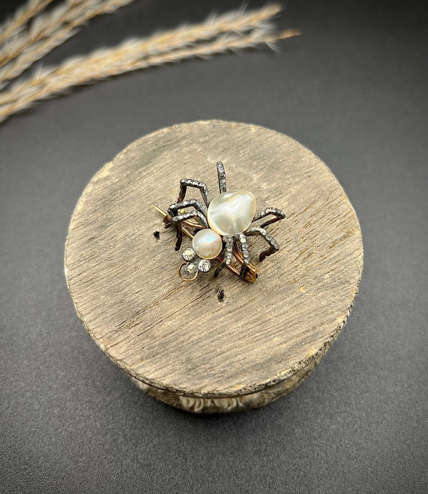 A pearl and diamond spider brooch in gold and silver, on a wooden spool