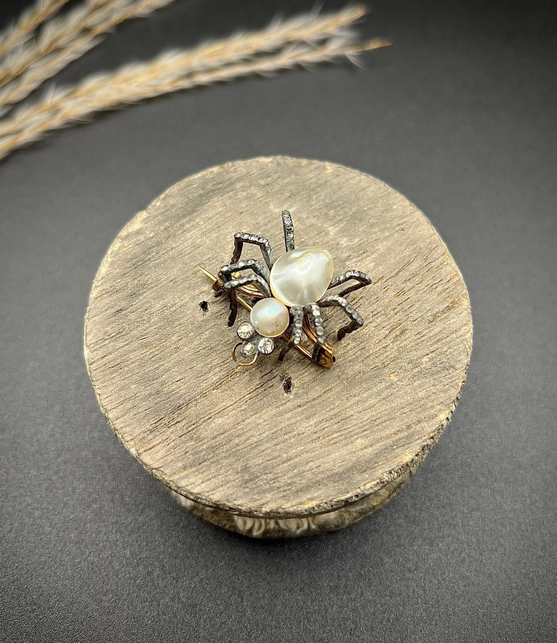 A pearl and diamond spider brooch in gold and silver, on a wooden spool