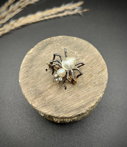 A pearl and diamond spider brooch in gold and silver, on a wooden spool