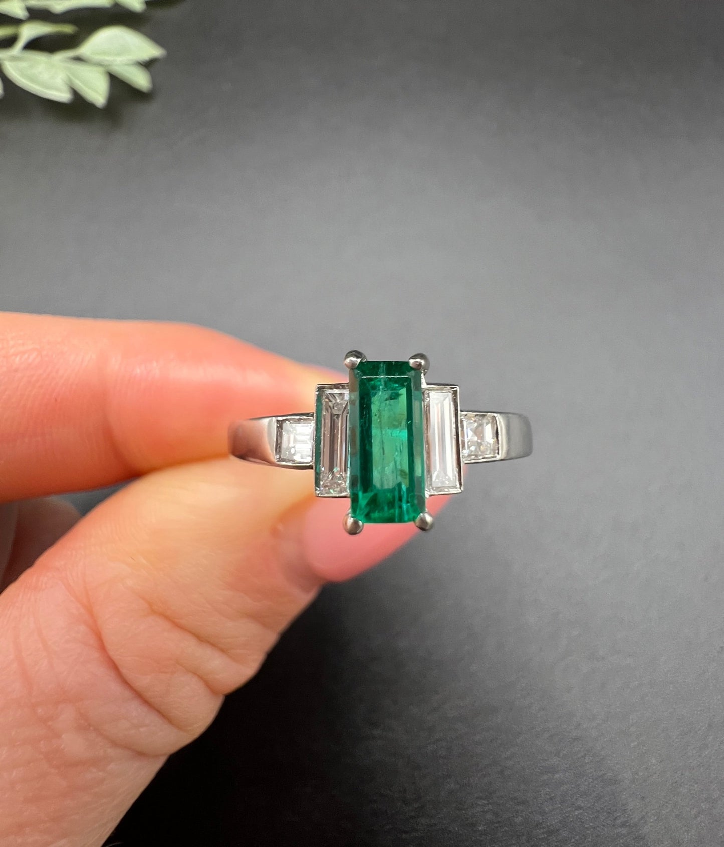 A five stone emerald cut emerald and baguette and square cut diamond ring in platinum, held in a hand