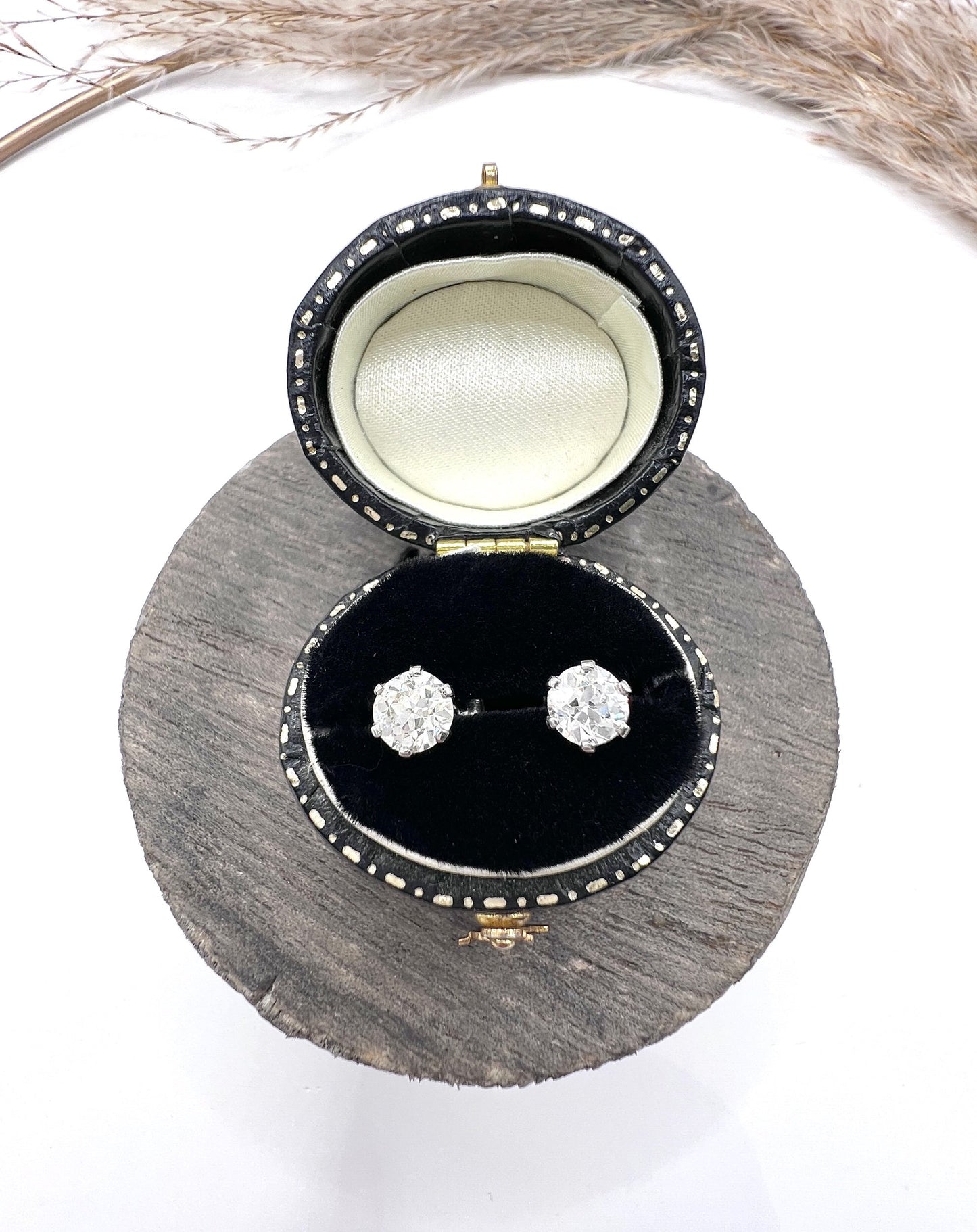 A pair of single stone round diamond stud earrings claw set in platinum, in a black jewellery box