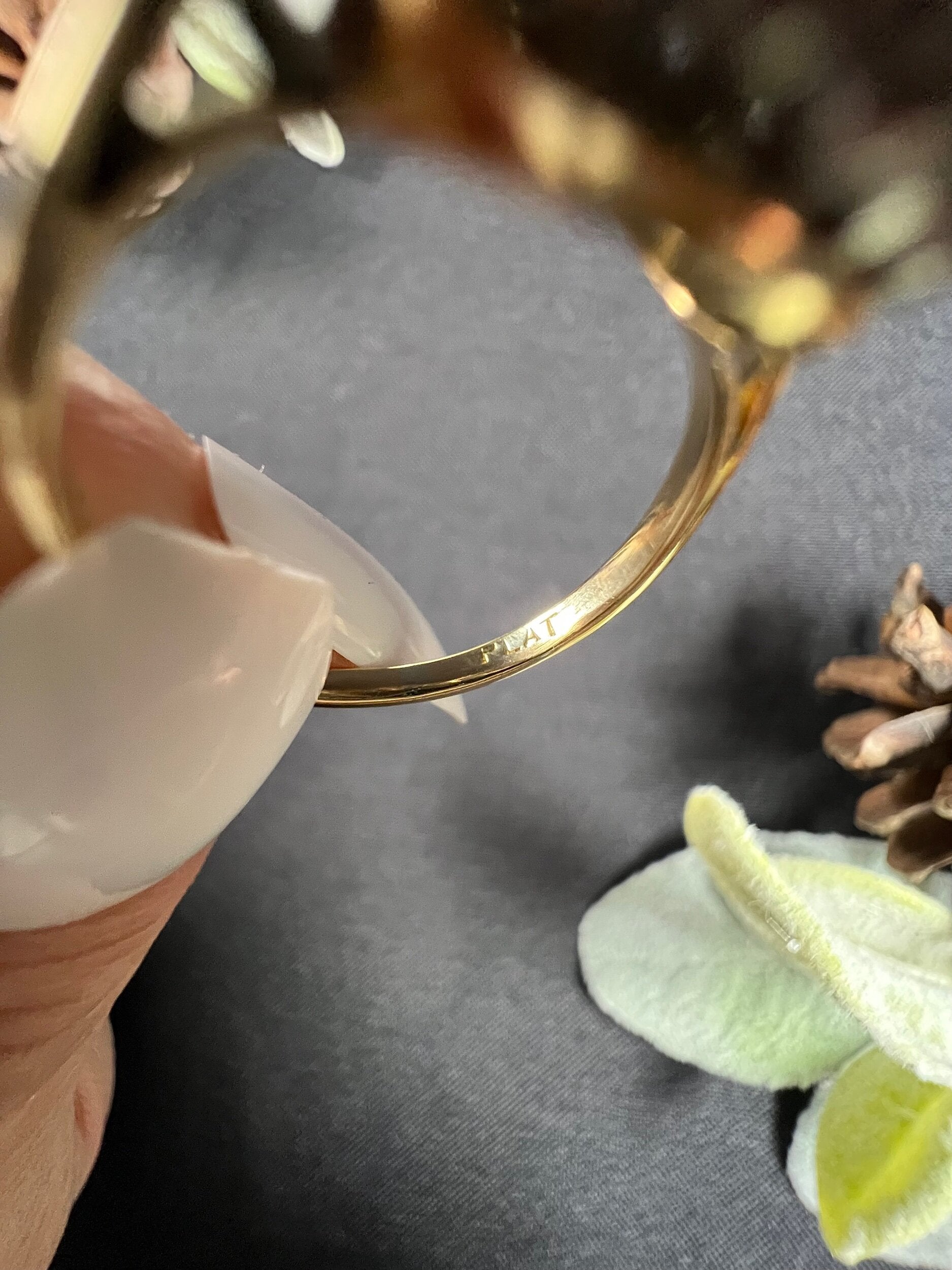 A close-up of a PLAT stamp inside a gold ring shank, held in a hand