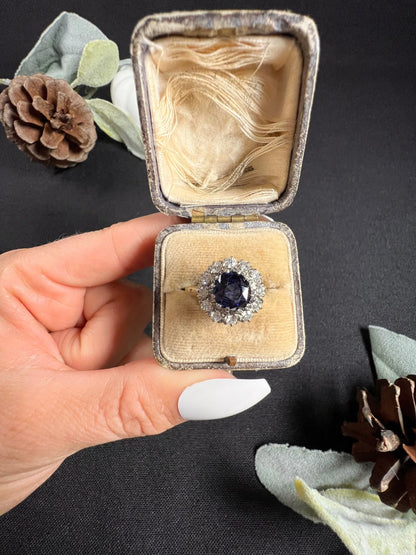 A round sapphire and diamond cluster ring, in an antique ring box, held by a hand