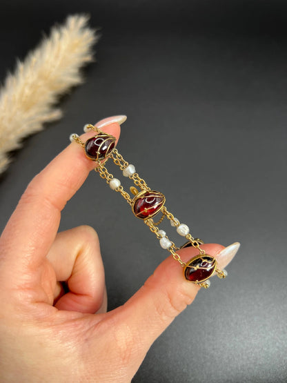 A yellow gold bracelet with oval cabochon garnets and white pearls, held in a hand