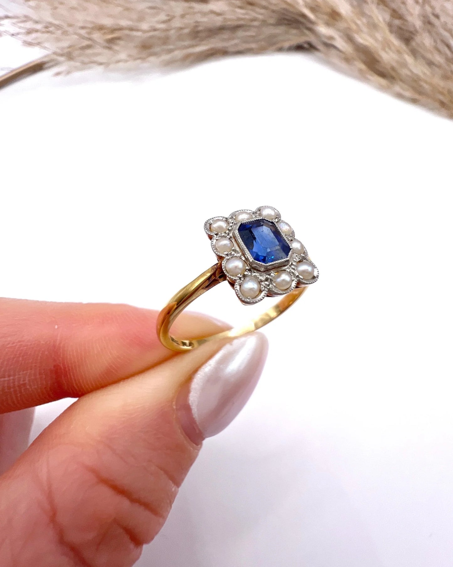 A sapphire and pearl cluster ring in yellow gold and platinum, held in a hand