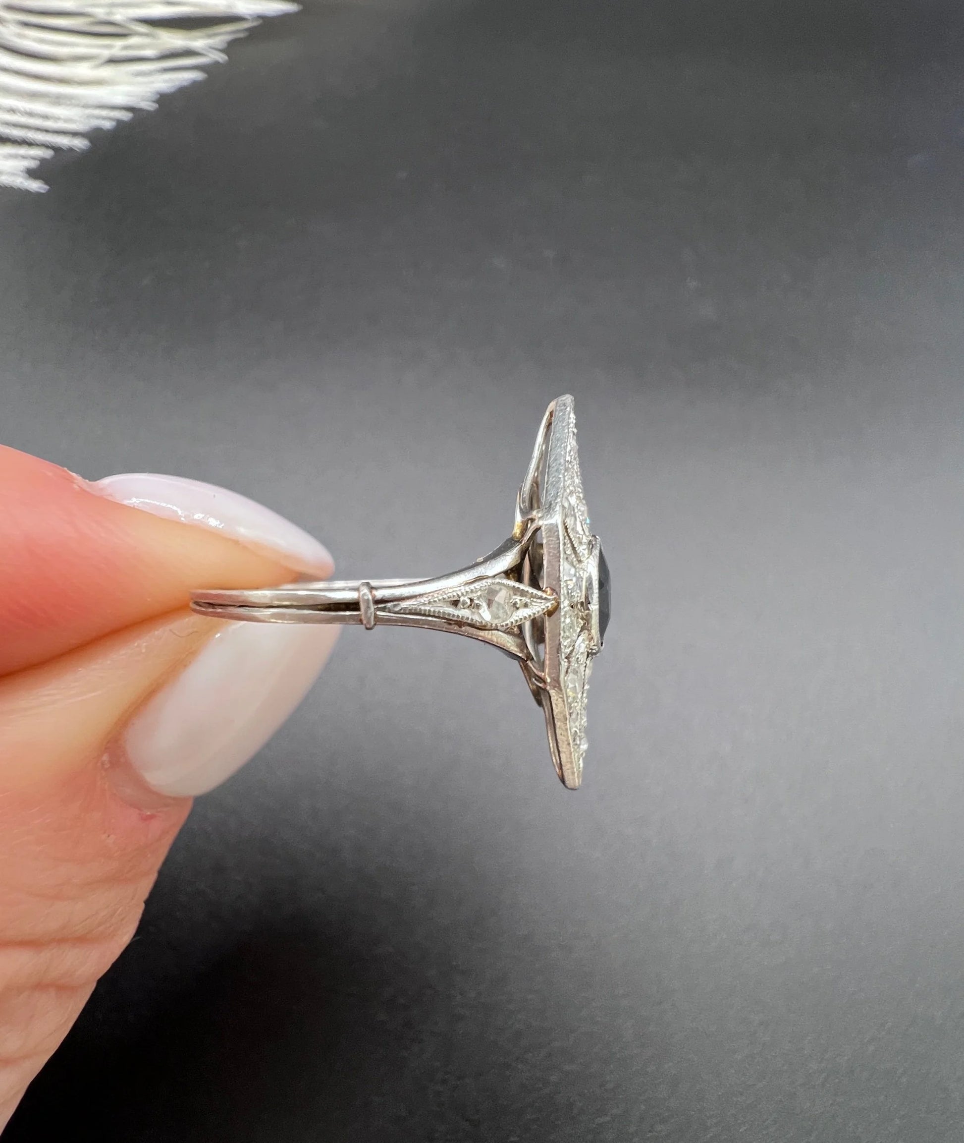 A navette shaped cluster cocktail ring with a sapphire centre surrounded by diamonds, in platinum, held in a hand