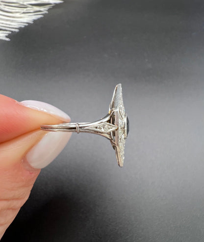 A navette shaped cluster cocktail ring with a sapphire centre surrounded by diamonds, in platinum, held in a hand