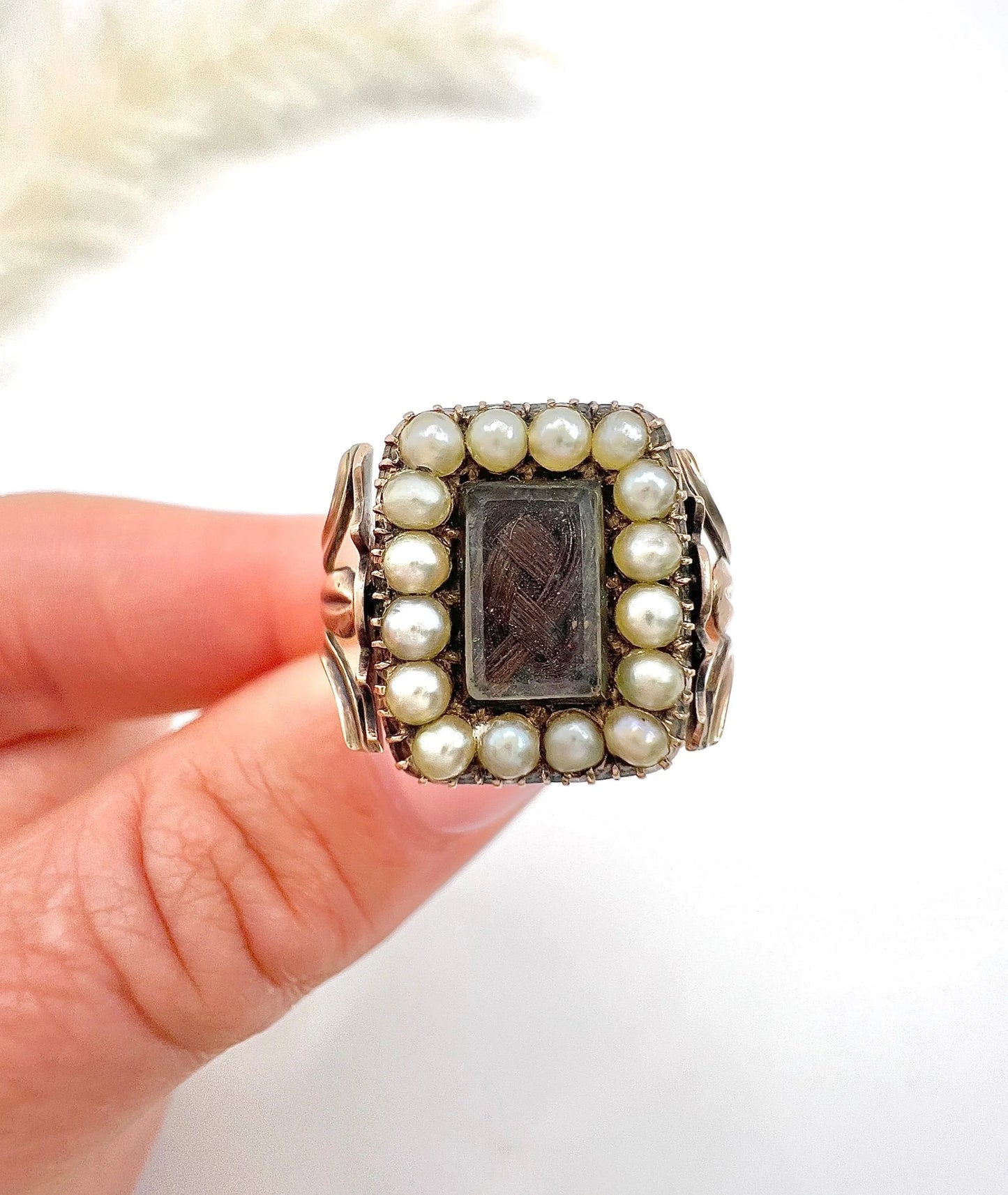 An antique seed pearl mourning ring in gold held in a hand