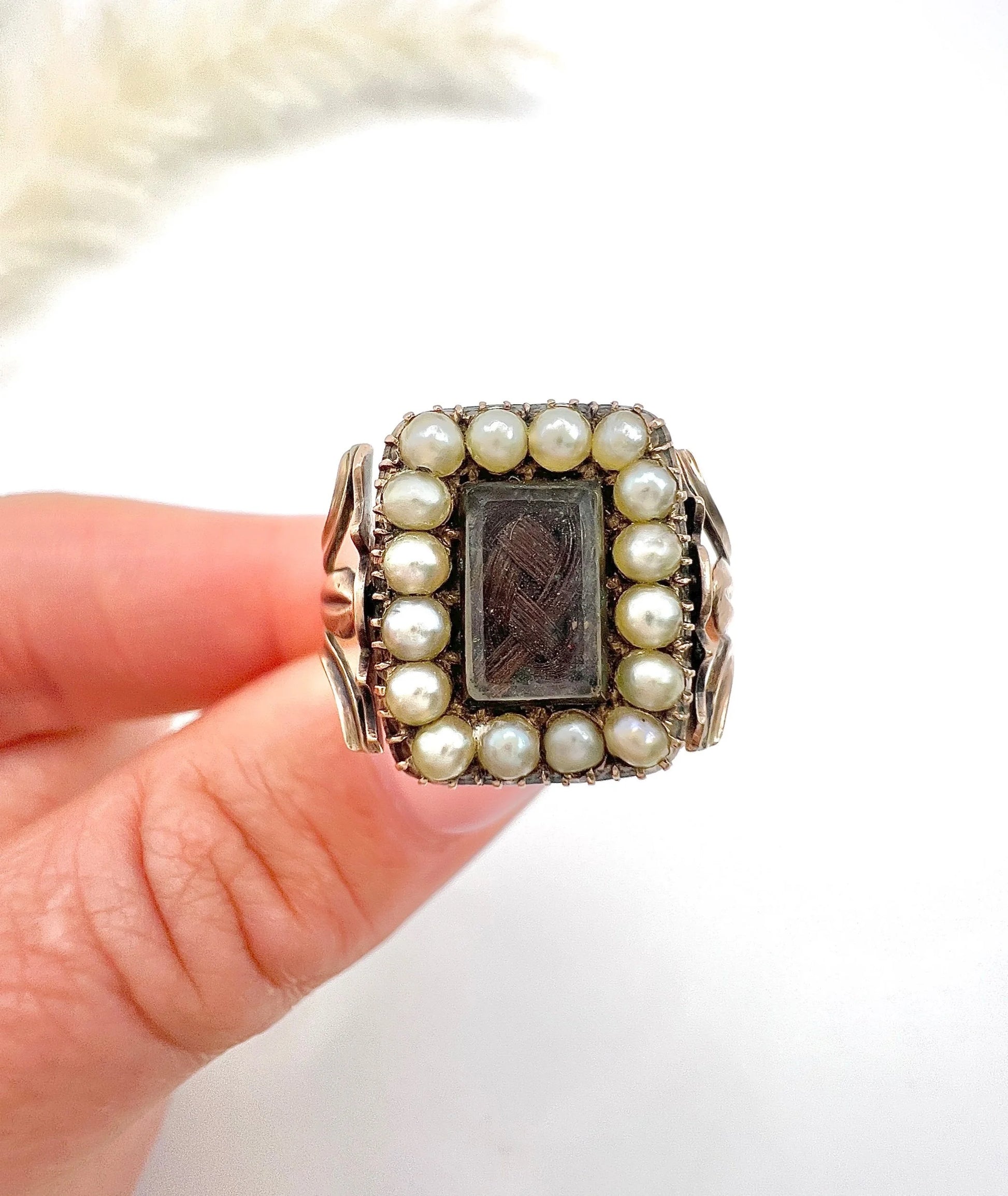 An antique seed pearl mourning ring in gold held in a hand
