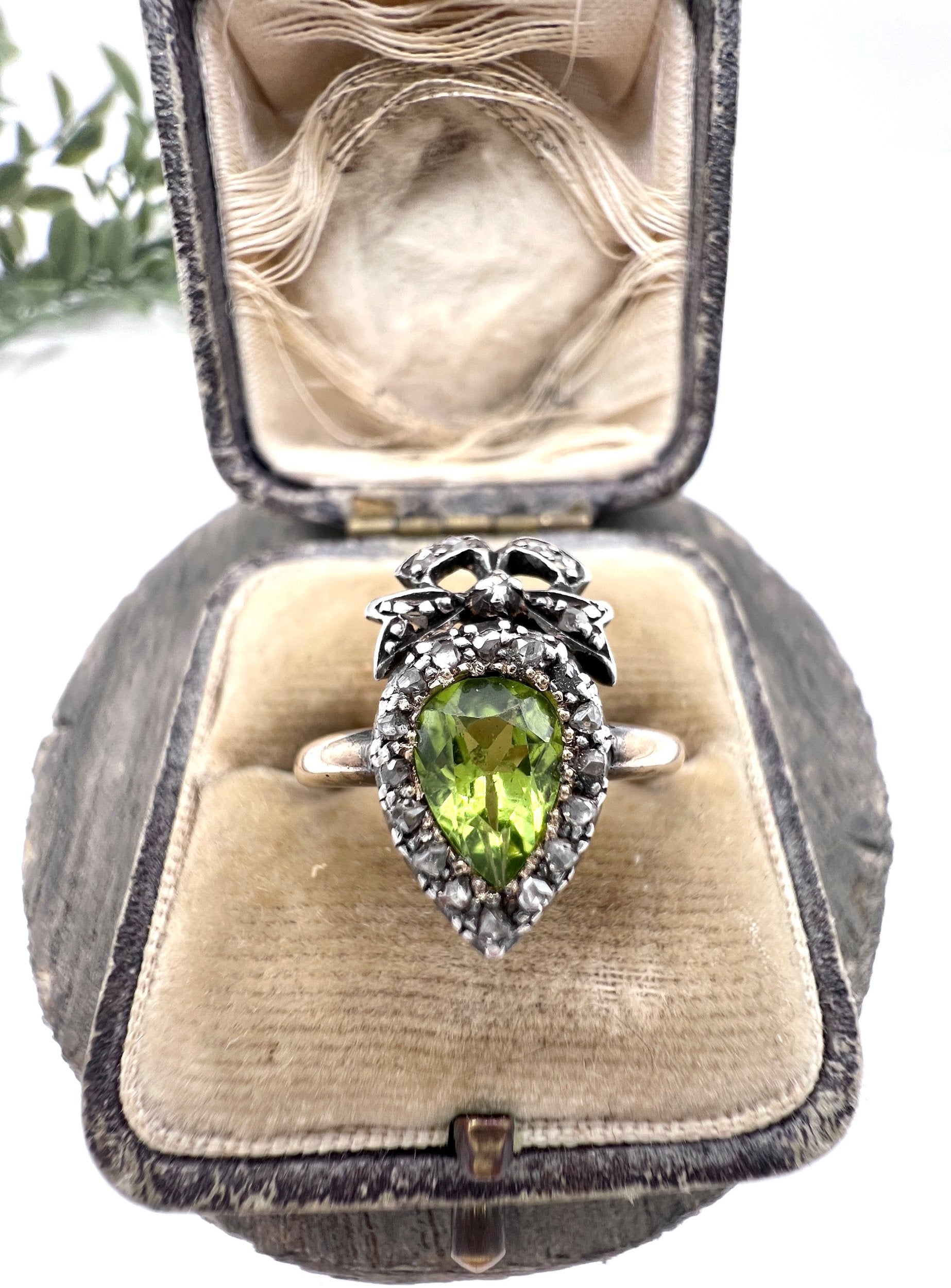 A pear cut peridot and round diamond cluster ring with bow detail, in yellow gold and white metal, in a ring box