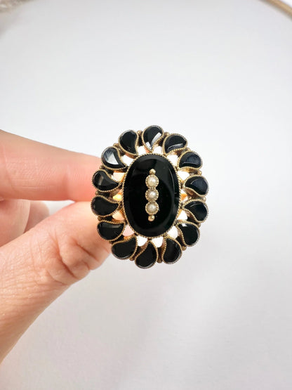 A black onyx and seed pearl fancy halo cluster ring in yellow gold, held in a hand