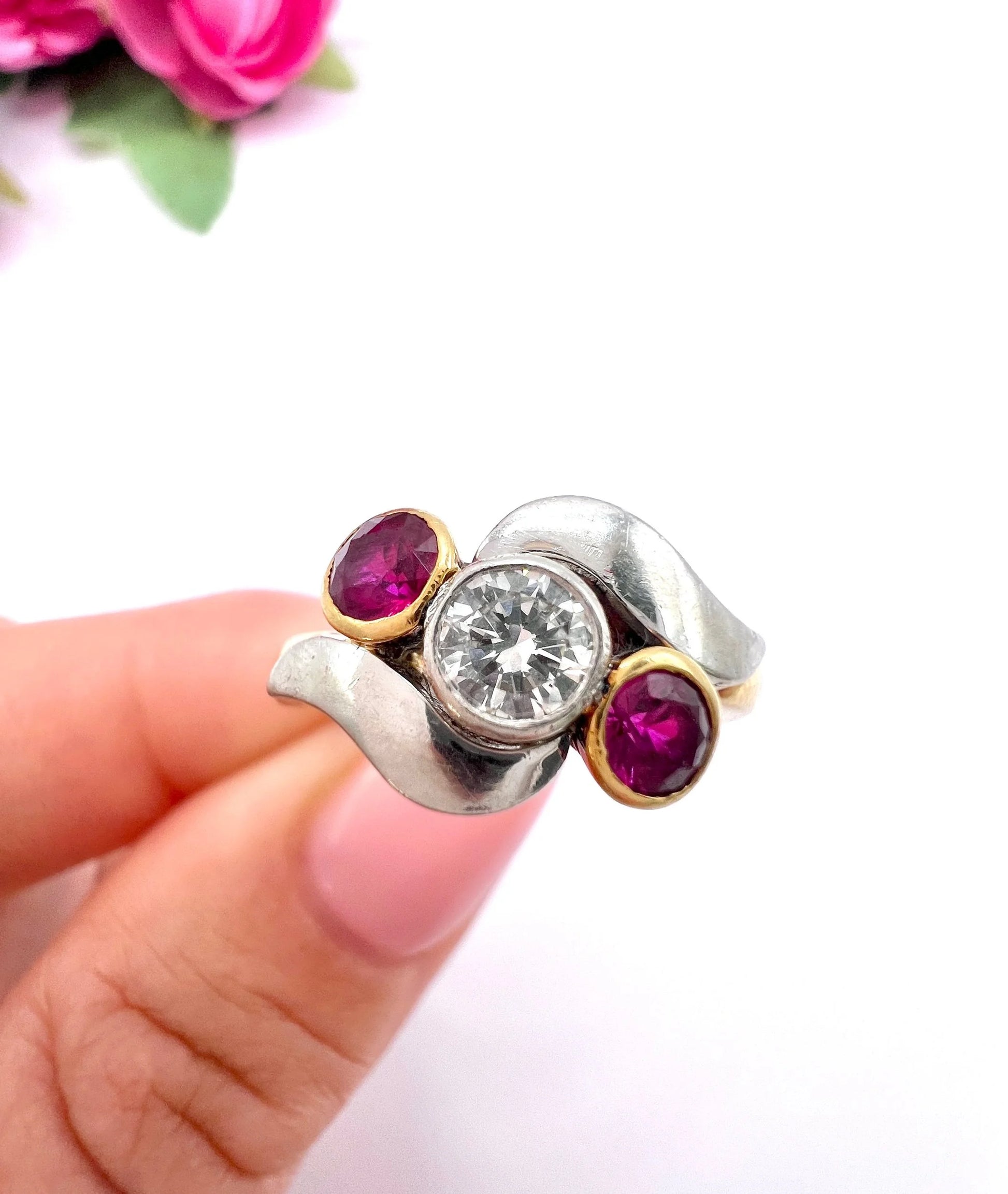 A three stone ruby and diamond crossover ring in platinum and yellow gold, held in a hand
