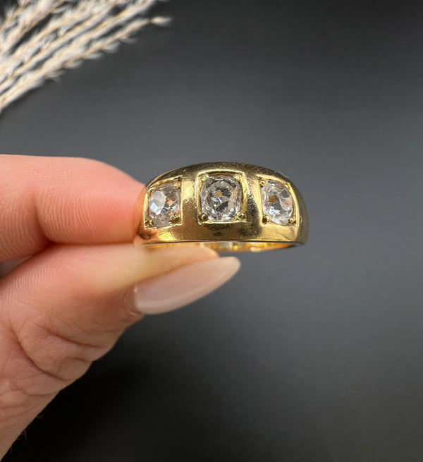 A three stone old cut diamond ring in yellow gold, held in a hand