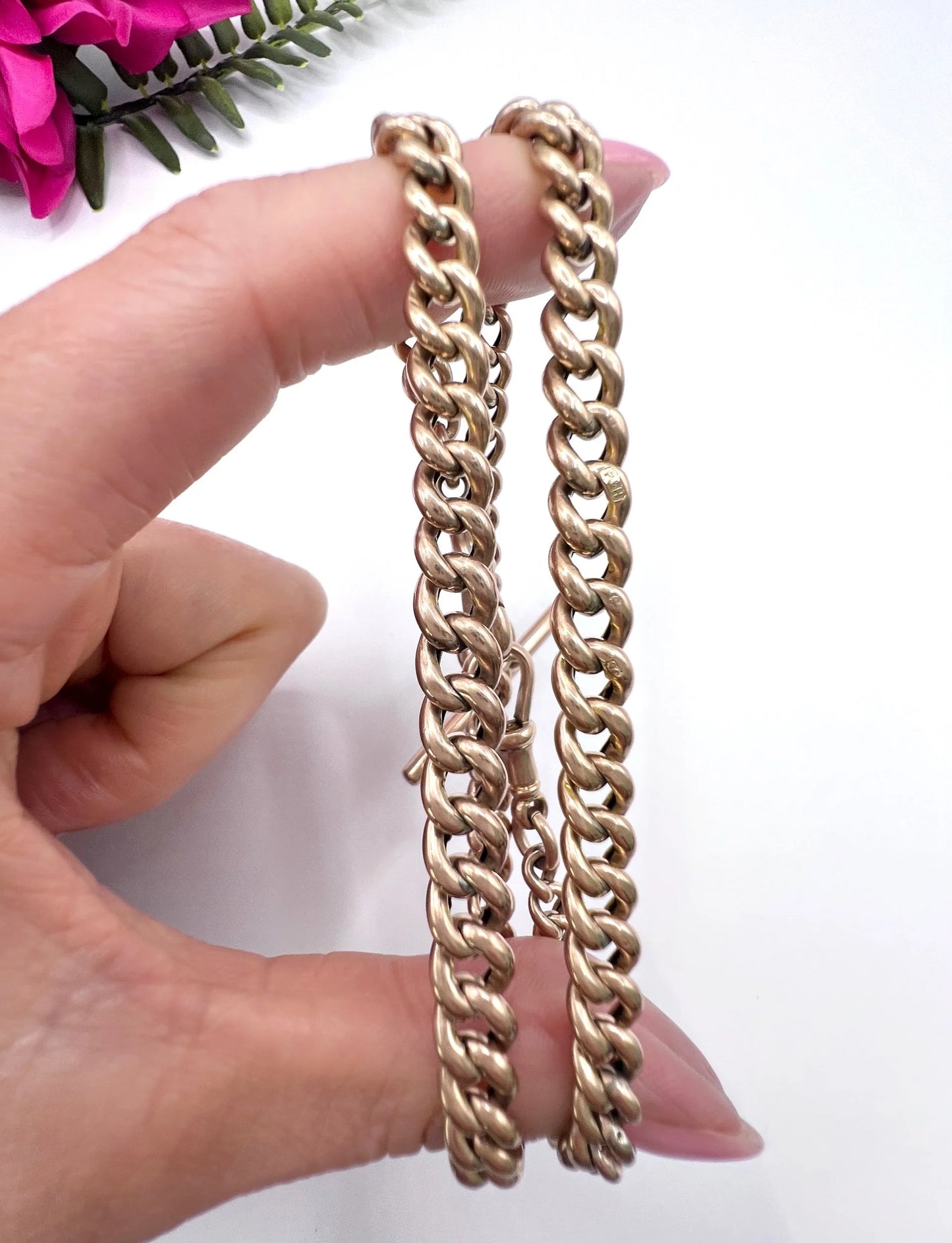 A rose gold curb link Albert chain with t-bar, held in a hand